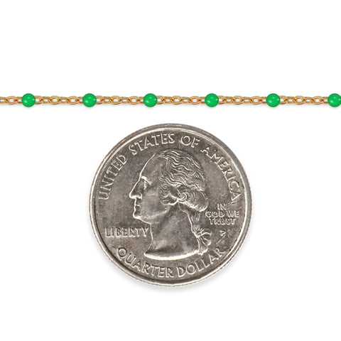 Gold chain with green beads next to a quarter on a white background