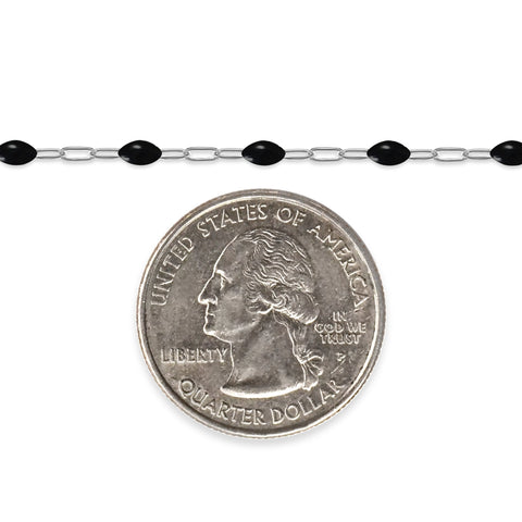 Silver chain with black enamel next to a quarter on a white background