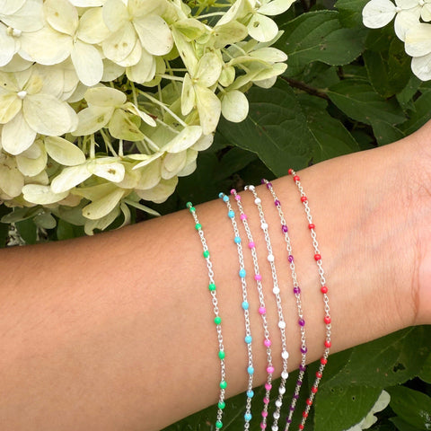 Close-up of a wrist with colorful sterling silver enamel chains against a background of white flowers and green leaves.