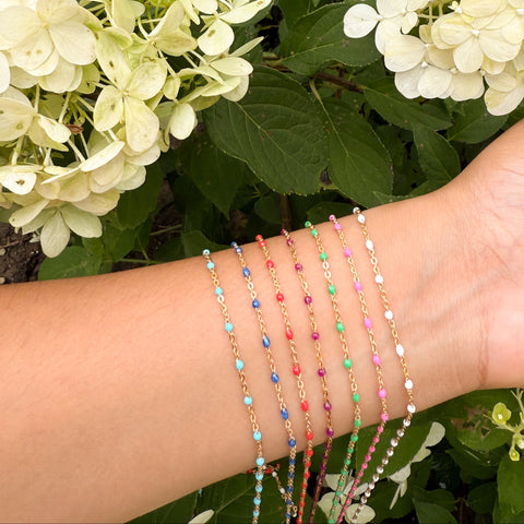 Wrist with colorful gold filled chains against a background of green foliage